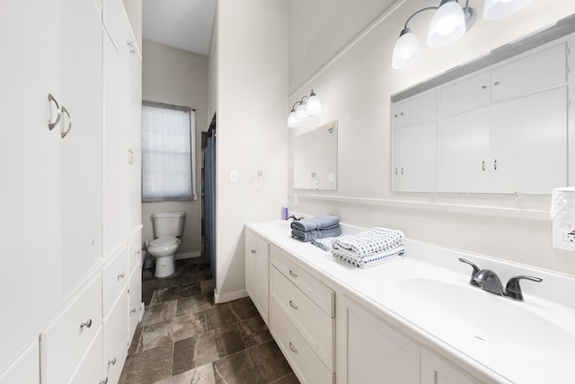 full bath with stone finish floor, toilet, vanity, and baseboards