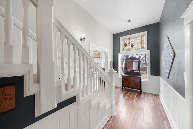 foyer entrance featuring a decorative wall, stairs, wainscoting, light wood-style flooring, and a notable chandelier