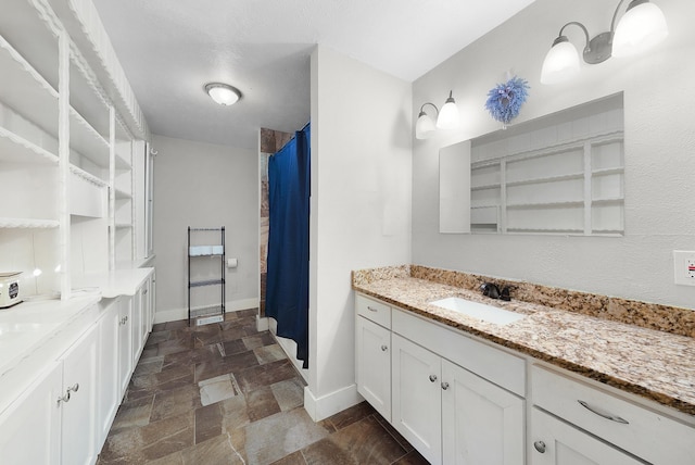 full bathroom featuring vanity, baseboards, and stone finish flooring