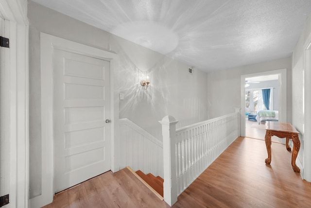 hallway with visible vents, an upstairs landing, a textured ceiling, and wood finished floors