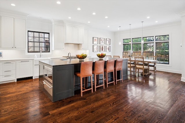 kitchen featuring ornamental molding, dark wood-type flooring, a sink, and an island with sink