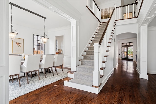 foyer entrance featuring arched walkways, dark wood-style floors, stairway, crown molding, and french doors