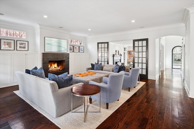 living room featuring a warm lit fireplace, dark wood-type flooring, arched walkways, and ornamental molding