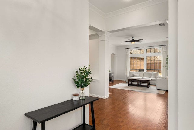 hallway featuring arched walkways, crown molding, visible vents, wood finished floors, and baseboards