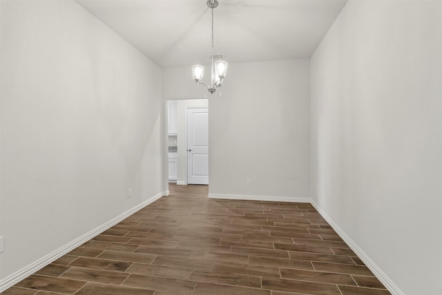 unfurnished dining area with an inviting chandelier, baseboards, and wood finish floors