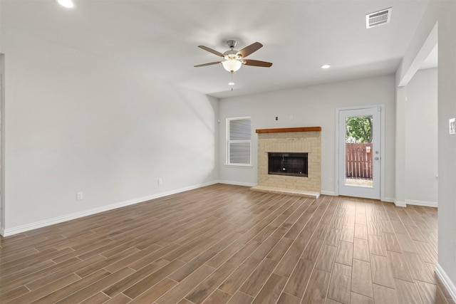 unfurnished living room featuring a fireplace, visible vents, ceiling fan, wood finished floors, and baseboards