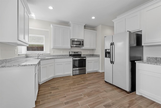 kitchen with stainless steel appliances, wood finish floors, a sink, and white cabinets