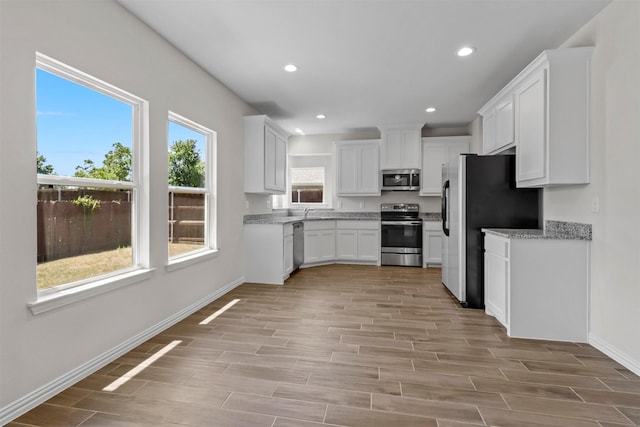 kitchen featuring recessed lighting, stainless steel appliances, wood finish floors, baseboards, and white cabinets