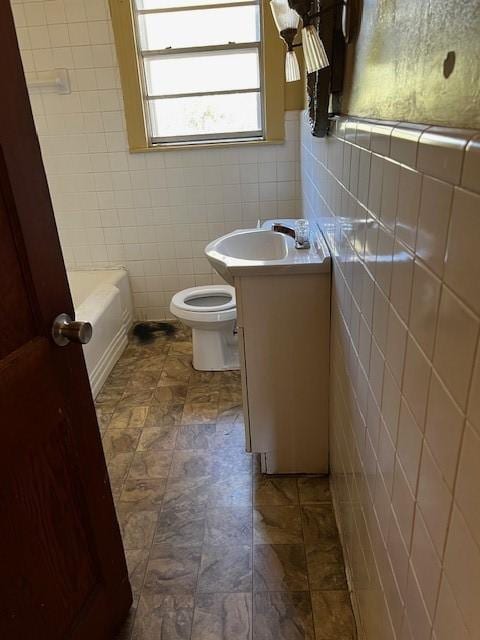 bathroom with a tub to relax in, tile walls, vanity, and toilet