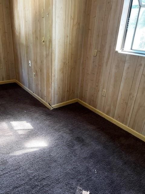 unfurnished room featuring dark colored carpet, wood walls, and baseboards