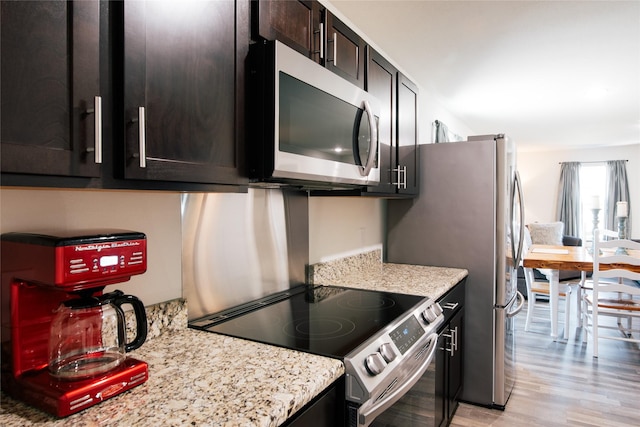 kitchen featuring stainless steel appliances, light stone counters, and light wood finished floors