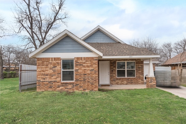 view of front of house featuring a front yard, a patio, fence, roof with shingles, and brick siding