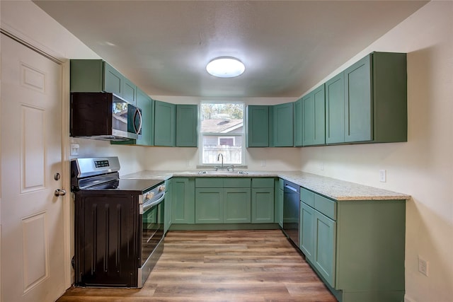 kitchen with appliances with stainless steel finishes, light countertops, light wood-type flooring, green cabinets, and a sink