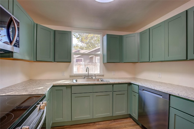 kitchen featuring a sink, light wood-type flooring, stainless steel appliances, and green cabinetry