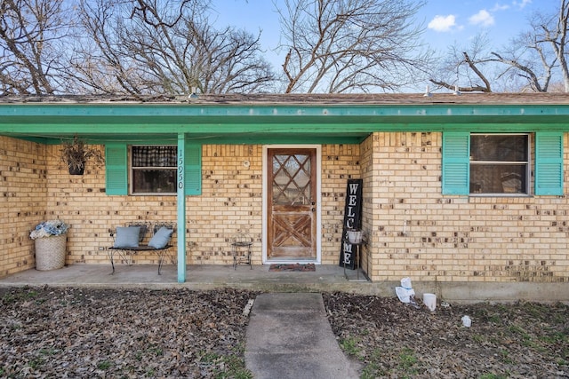 doorway to property featuring covered porch and brick siding