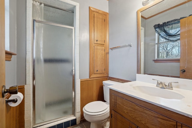 bathroom with a stall shower, wainscoting, vanity, and toilet