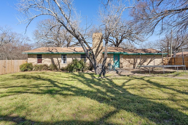 back of property with a trampoline, a fenced backyard, brick siding, and a lawn