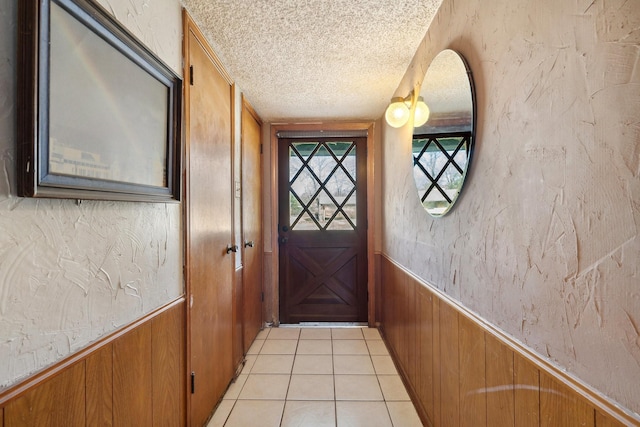 entryway with a textured ceiling, a textured wall, light tile patterned floors, wood walls, and wainscoting