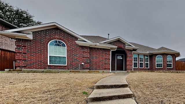 ranch-style home featuring roof with shingles, fence, a front lawn, and brick siding