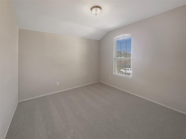 carpeted empty room featuring lofted ceiling and baseboards