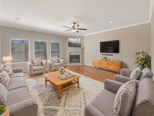 living room featuring wood finished floors, a ceiling fan, visible vents, a glass covered fireplace, and crown molding