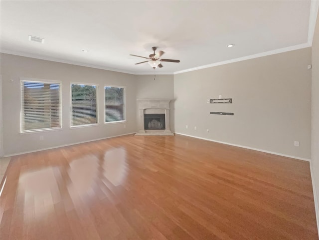 unfurnished living room with baseboards, visible vents, a ceiling fan, a glass covered fireplace, and ornamental molding