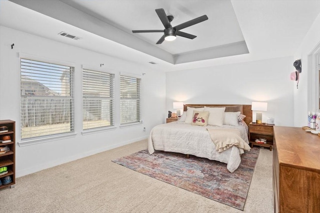 carpeted bedroom with visible vents, a raised ceiling, baseboards, and ceiling fan