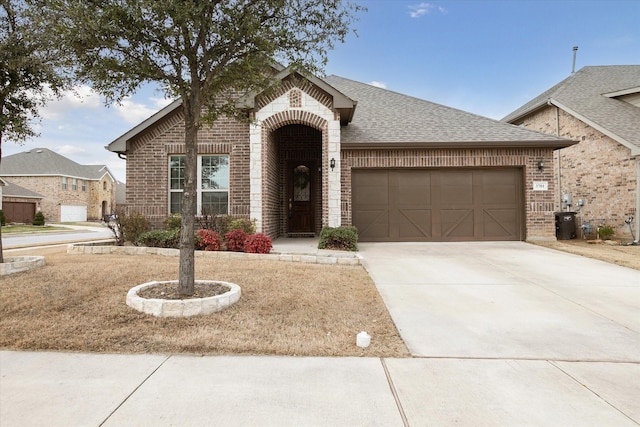 view of front of home featuring driveway, a shingled roof, a garage, and brick siding