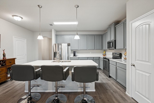 kitchen with a center island with sink, dark wood finished floors, appliances with stainless steel finishes, gray cabinets, and a sink