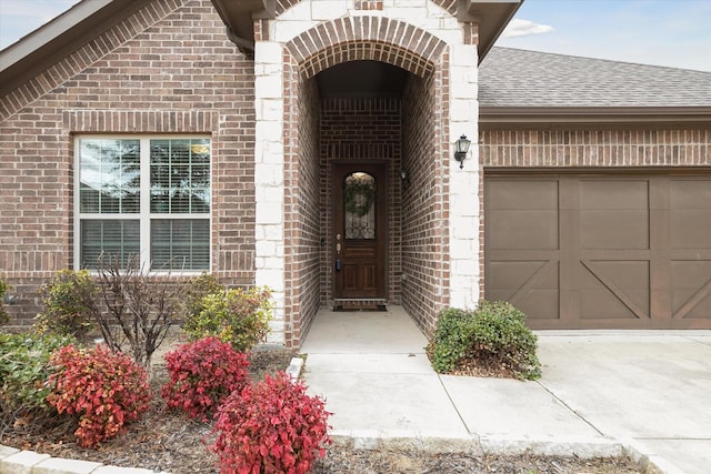 entrance to property featuring a garage, driveway, a shingled roof, and brick siding