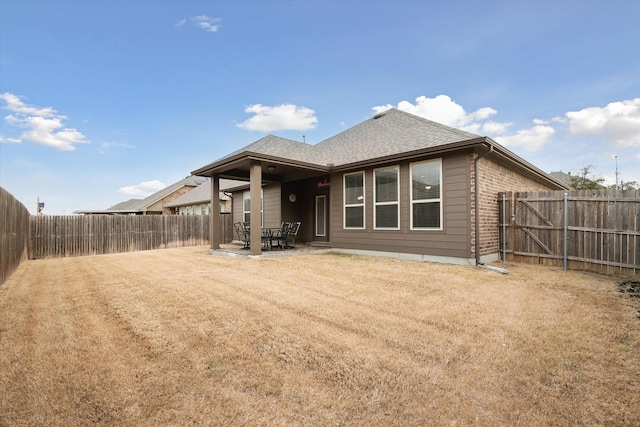 rear view of house with a patio area, a fenced backyard, a shingled roof, and brick siding