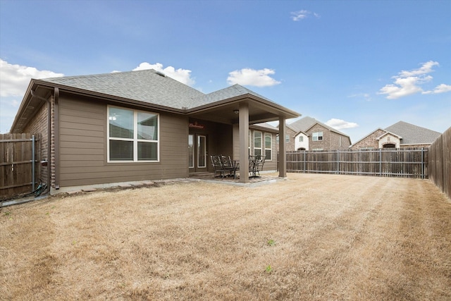 back of house with a patio area, a fenced backyard, roof with shingles, and brick siding