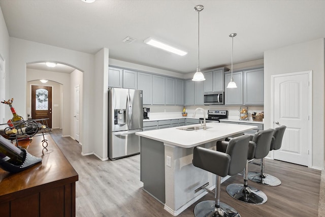 kitchen with arched walkways, stainless steel appliances, gray cabinets, a sink, and light wood-type flooring