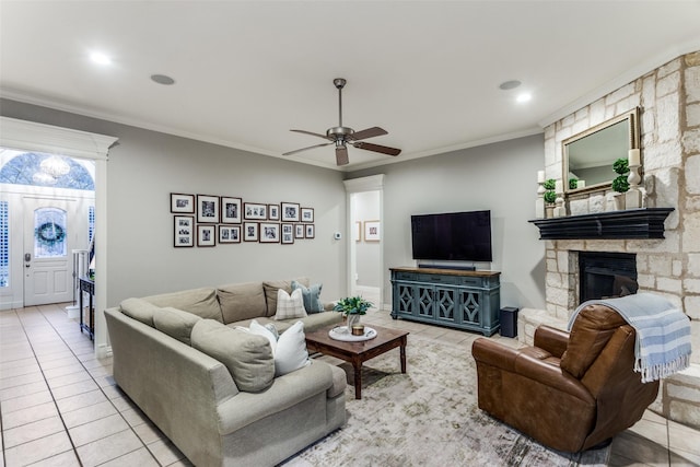 living room with a ceiling fan, light tile patterned flooring, crown molding, and a stone fireplace