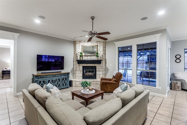 living area with light tile patterned floors, ceiling fan, a stone fireplace, baseboards, and ornamental molding