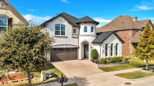 french provincial home with roof with shingles, stucco siding, an attached garage, stone siding, and driveway