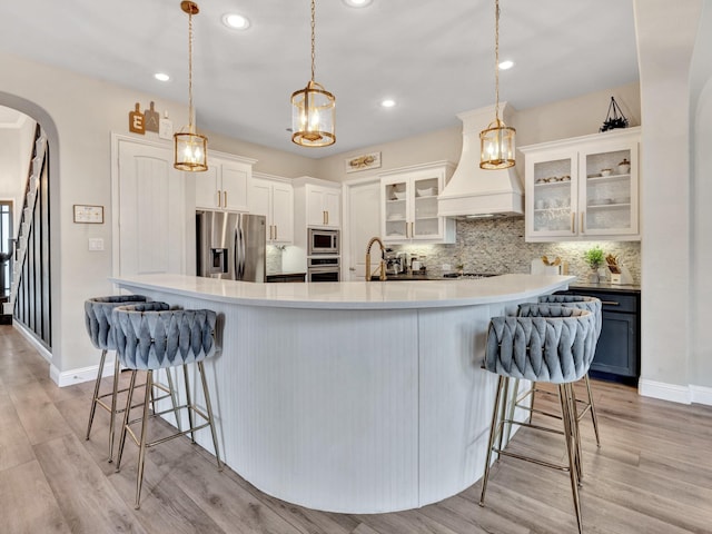 kitchen featuring arched walkways, decorative backsplash, a breakfast bar area, appliances with stainless steel finishes, and premium range hood