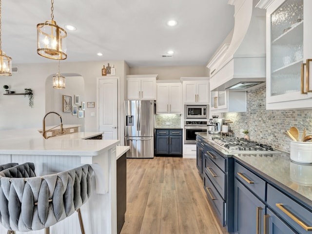 kitchen featuring white cabinets, appliances with stainless steel finishes, custom exhaust hood, light wood-type flooring, and backsplash