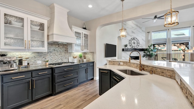 kitchen featuring white cabinets, a sink, hanging light fixtures, custom exhaust hood, and backsplash