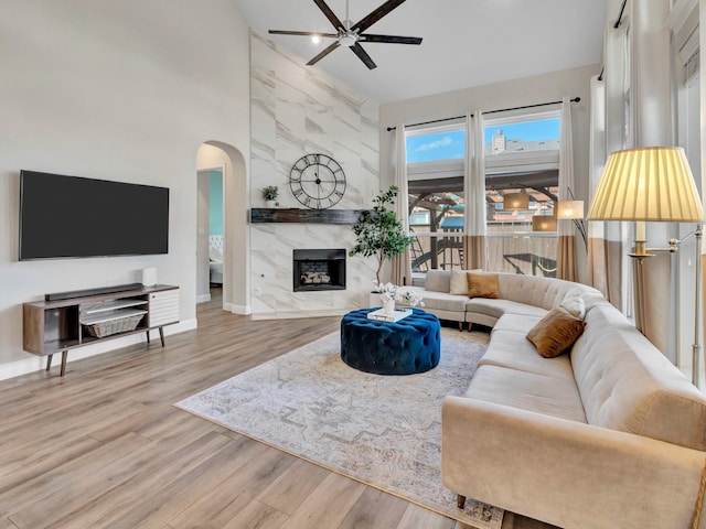 living area featuring arched walkways, a fireplace, ceiling fan, wood finished floors, and baseboards