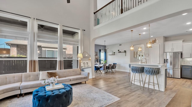 living room featuring recessed lighting, a towering ceiling, baseboards, light wood-type flooring, and an inviting chandelier