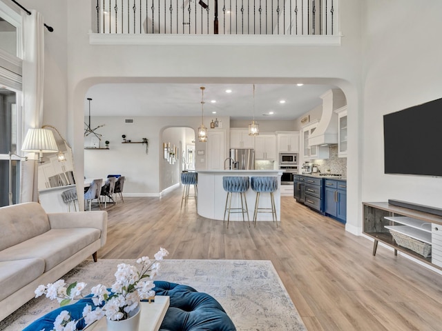 living area featuring light wood-style floors, arched walkways, a towering ceiling, and baseboards