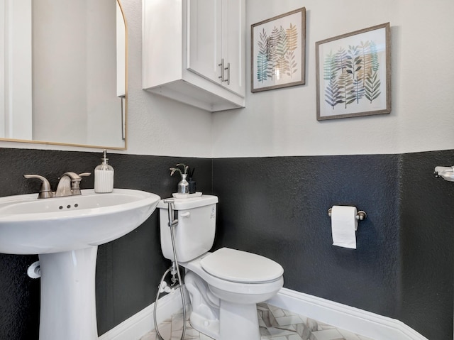 half bathroom featuring marble finish floor, baseboards, a textured wall, and toilet