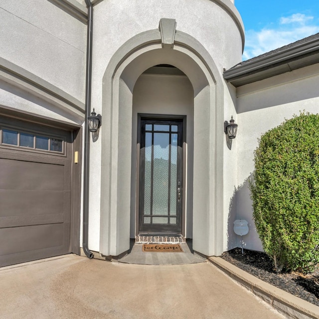 view of exterior entry with a garage, driveway, and stucco siding