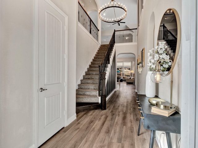 foyer entrance with a chandelier, arched walkways, stairway, and wood finished floors