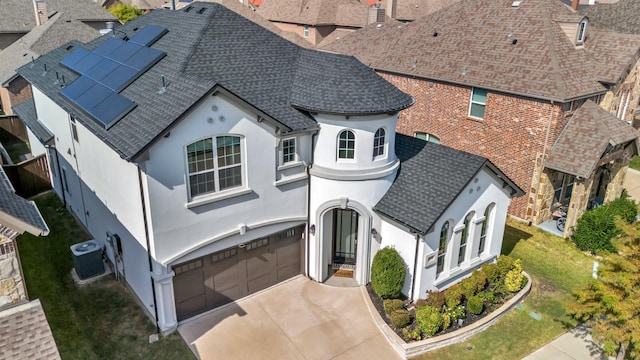 view of front of home featuring solar panels, a shingled roof, an attached garage, central AC, and driveway