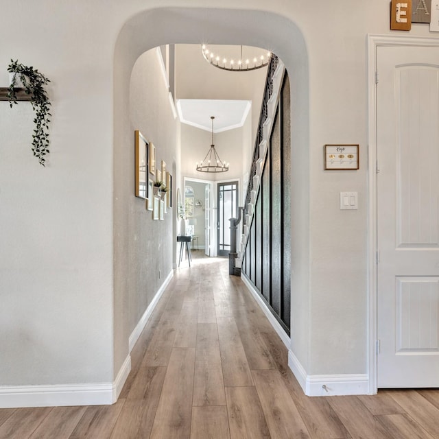 corridor with baseboards, arched walkways, ornamental molding, an inviting chandelier, and light wood-style floors