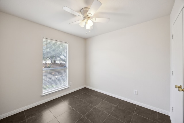 empty room with dark tile patterned floors, baseboards, and a ceiling fan