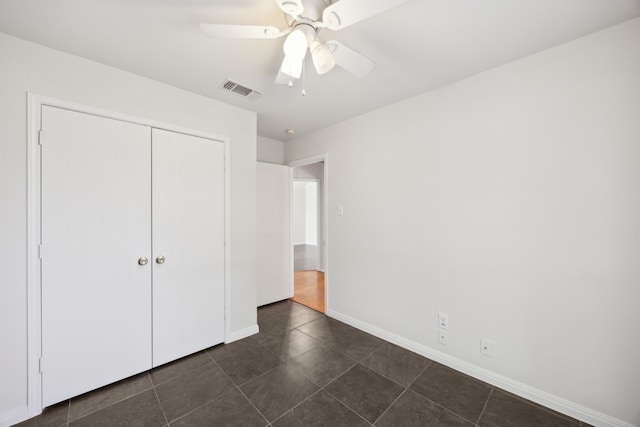 unfurnished bedroom with dark tile patterned floors, a closet, visible vents, and baseboards