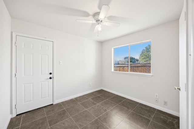 spare room featuring dark tile patterned floors, baseboards, and a ceiling fan